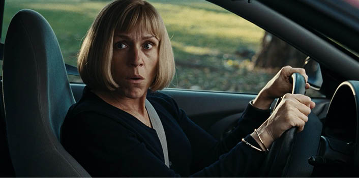 A woman is sitting in a car, wearing a black shirt and a seatbelt. Description generated by AI