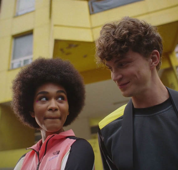 A man and a woman standing in front of a yellow building. Description generated by AI