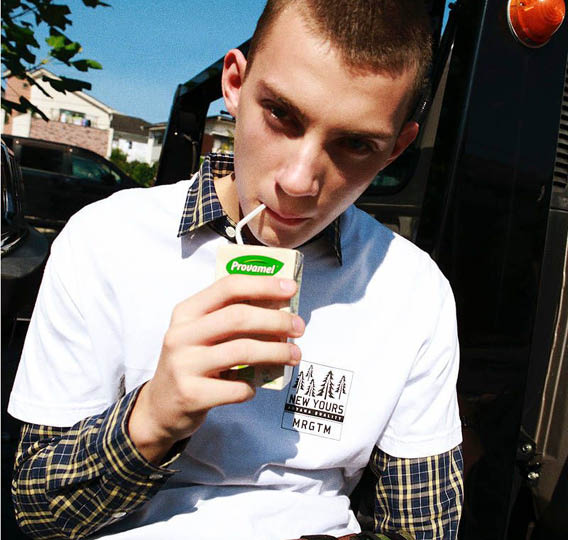 A man wearing a white shirt and a camouflage backpack drinking a green juice. Description generated by AI